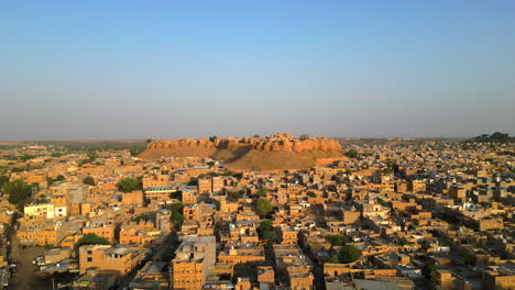 una impresionante toma lateral de drone del fuerte de jaisalmer en rajasthan, india, que destaca su majestuosa arquitectura rodeada de casas de tonos dorados bajo el cielo brillante y soleado 4k