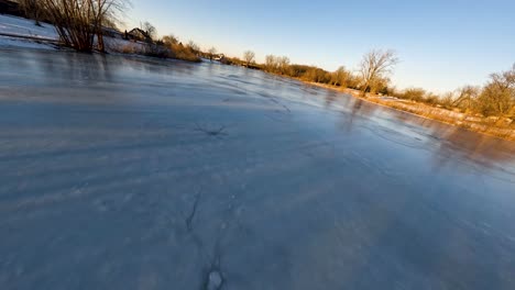 fast drone flying above a frozen pond in michigan during sunset