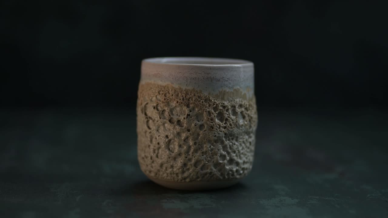 Purring a water into a ceramic glass with volcano texture on the dark background