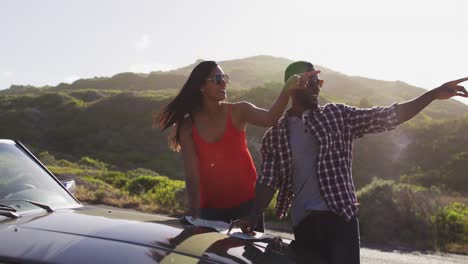 Pareja-Afroamericana-Usando-Mapas-Para-Obtener-Direcciones-Mientras-Está-De-Pie-Cerca-De-Un-Auto-Convertible-En-La-Carretera