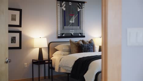 modern bedroom with warm lighting, a made bed, nightstands, and decorative pillows beneath a patterned wall hanging