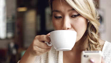 Mujer-Asiática-Usando-La-Pantalla-Táctil-Del-Teléfono-Inteligente-En-La-Cafetería-Bebiendo-Café