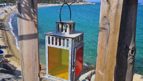 Empty-Colorful-Lantern-Hanging-on-Wooden-Fence-Above-Mediterranean-Beach-on-Sunny-Day,-Close-Up