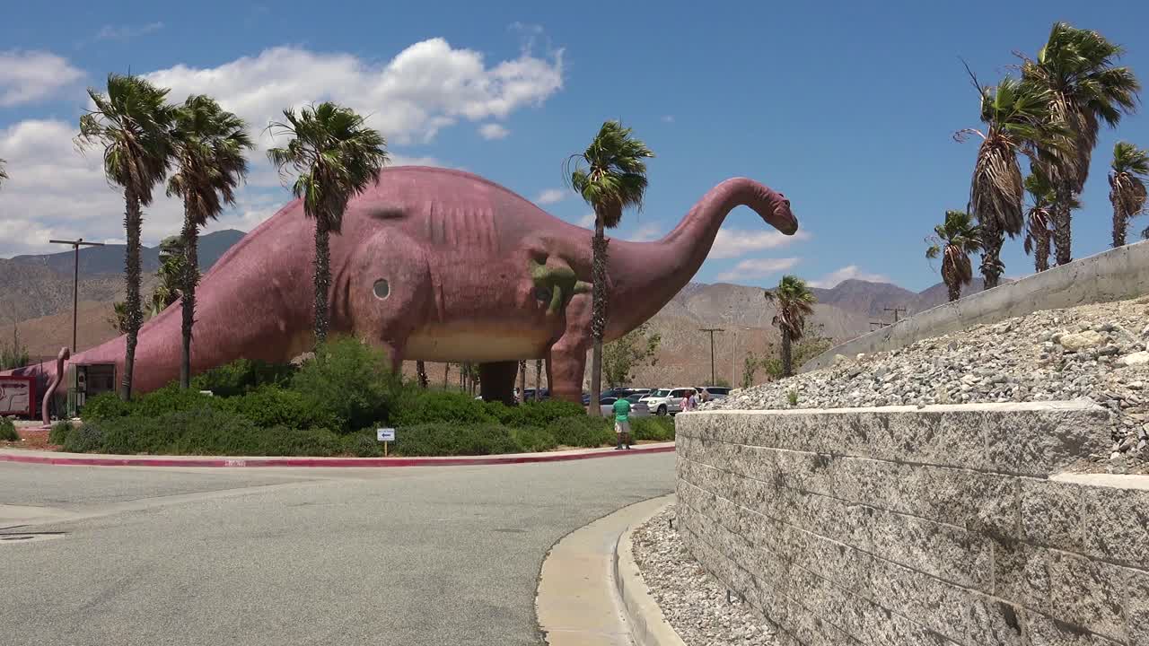 cabazon california 1 근처의 모하비 사막에 있는 길가 명소로 방문객들 위에 거대한 인공 공룡이 어렴풋이 보입니다.