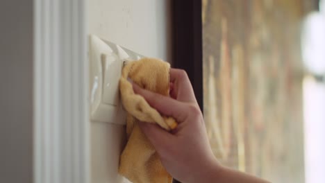 hand rubbing and cleaning light switches for disinfection from virus with orange microfiber