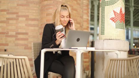 Woman-talking-on-smartphone-while-working-with-laptop-in-cafe