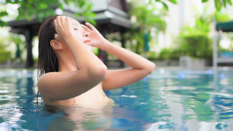 Mientras-Se-Pasa-El-Dedo-Por-Su-Largo-Cabello-Mojado,-Una-Hermosa-Joven-Disfruta-De-Las-Aguas-De-La-Piscina-De-Su-Hotel-De-Lujo