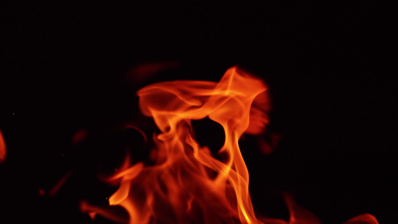Flame of bonfire moving to the sides in the wind. Beautiful orange fire at black backdrop. Close up.