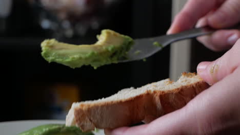 spreading fresh avocado on a bread toast for breakfast - close up