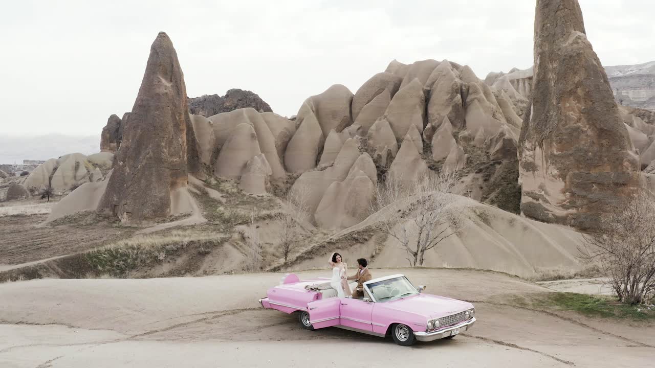 una pareja en un coche vintage rosa en capadocia.