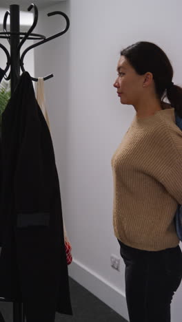 vertical video of woman getting home from food shopping hanging up coat and carrying bag of fresh vegetables indoors into kitchen 1