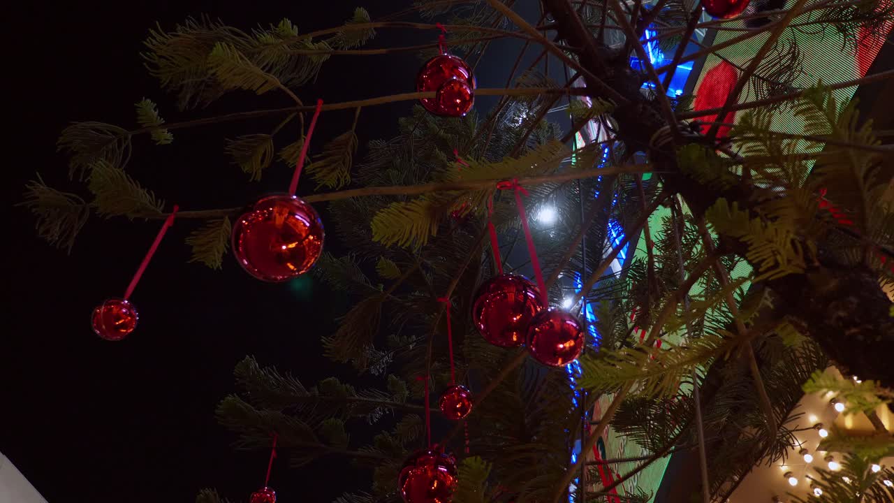 árbol de navidad decorado con bolas rojas brillantes colgando de una cuerda, frente a un centro comercial comunitario en bangkok, tailandia