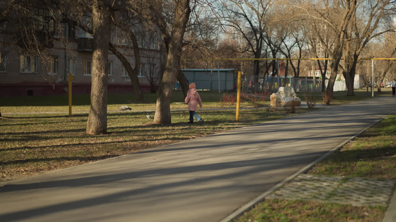 분홍색 모자와 재을 입은 작은 소녀는 파란 청바지를 입고 이 많은 공원 길에서 기게 비둘기를 고 있습니다.