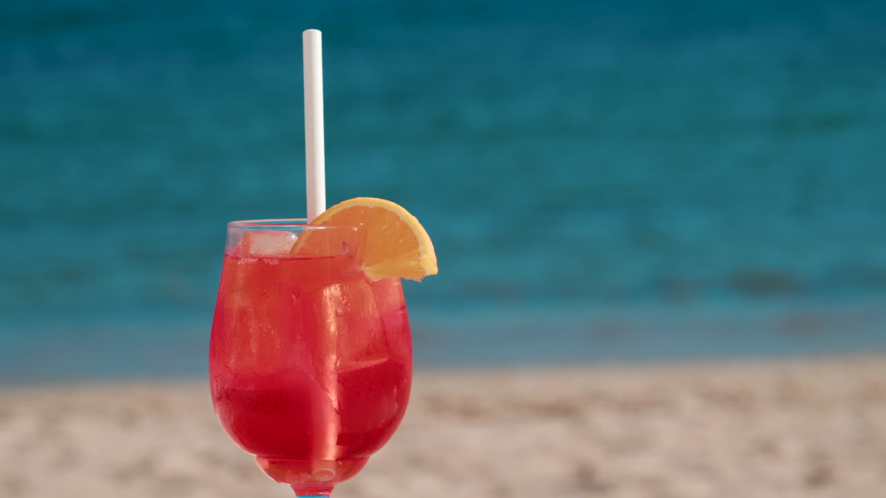 Refreshing red orange cocktail with ice and orange slice against the deep blue Mediterranean Sea