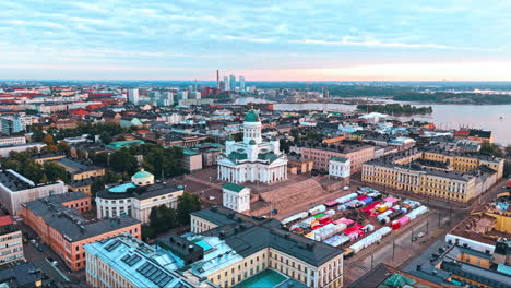 Helsinki-Cathedral-and-central-Helsinki-in-sunrise,-archipelago,-sea,-lake-and-forest-in-background,-camera-moving-downwards