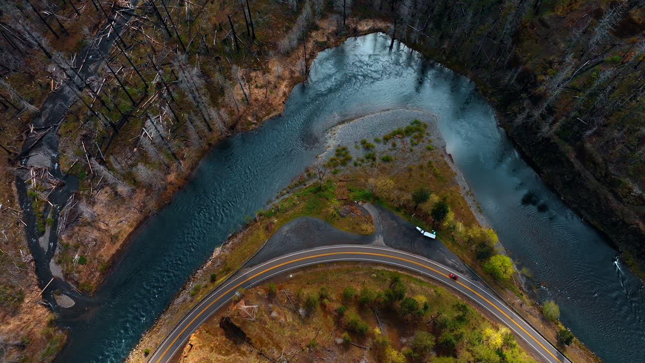 Rising over the river turn flowing through the mountainous area. Car moves around the rock by the wavy highway.