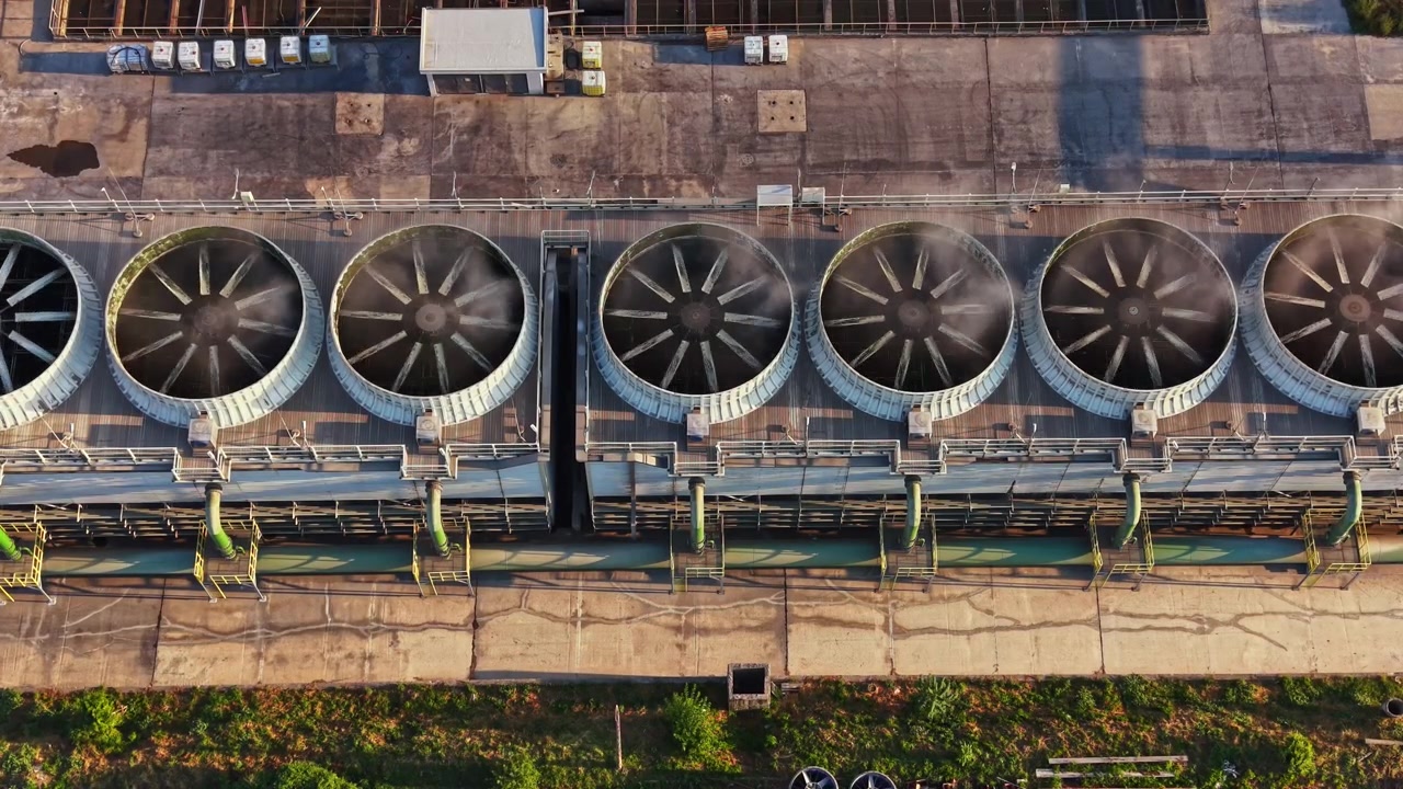 Large cooling towers on a factory roof with ventilation systems and pipes during daylight