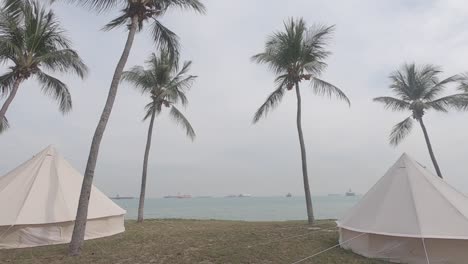 dos tiendas de campaña en la playa de palmeras con los buques de carga desde lejos en la vista del mar