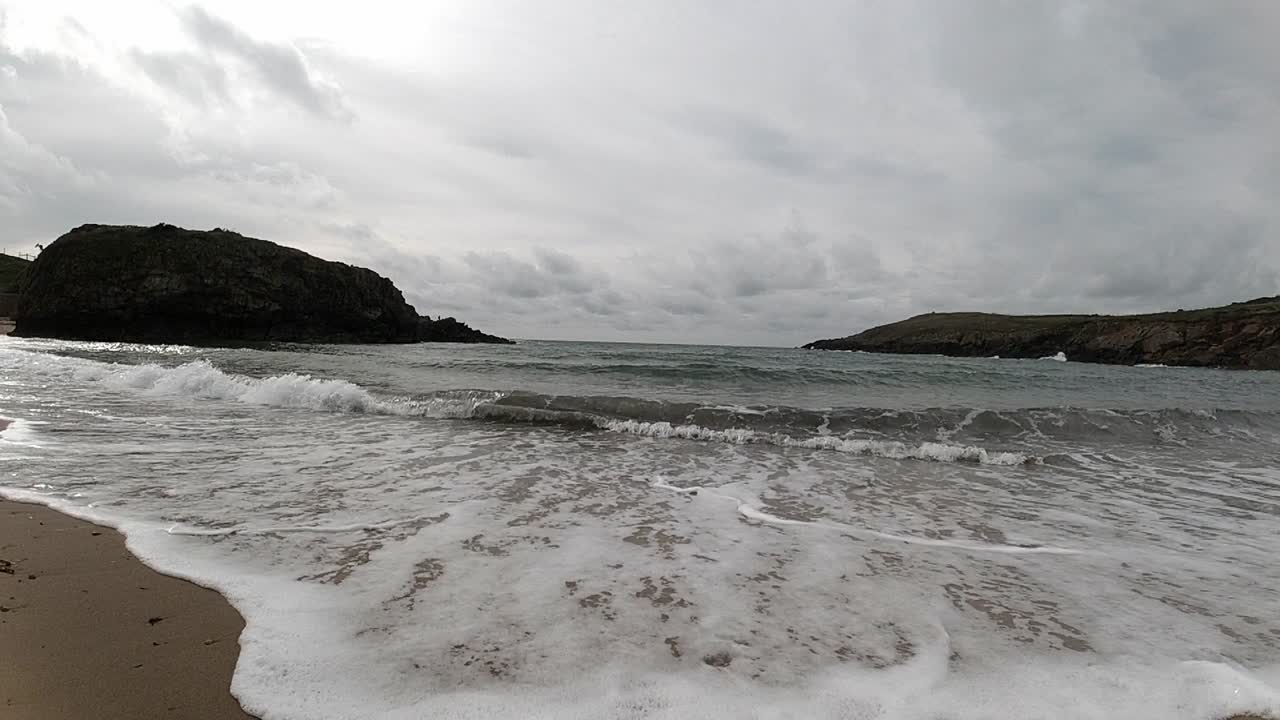 수평선을 가로질러 섬 산이 있는 모래 웨일스 해변에서 슬로우 모션 조수 세척