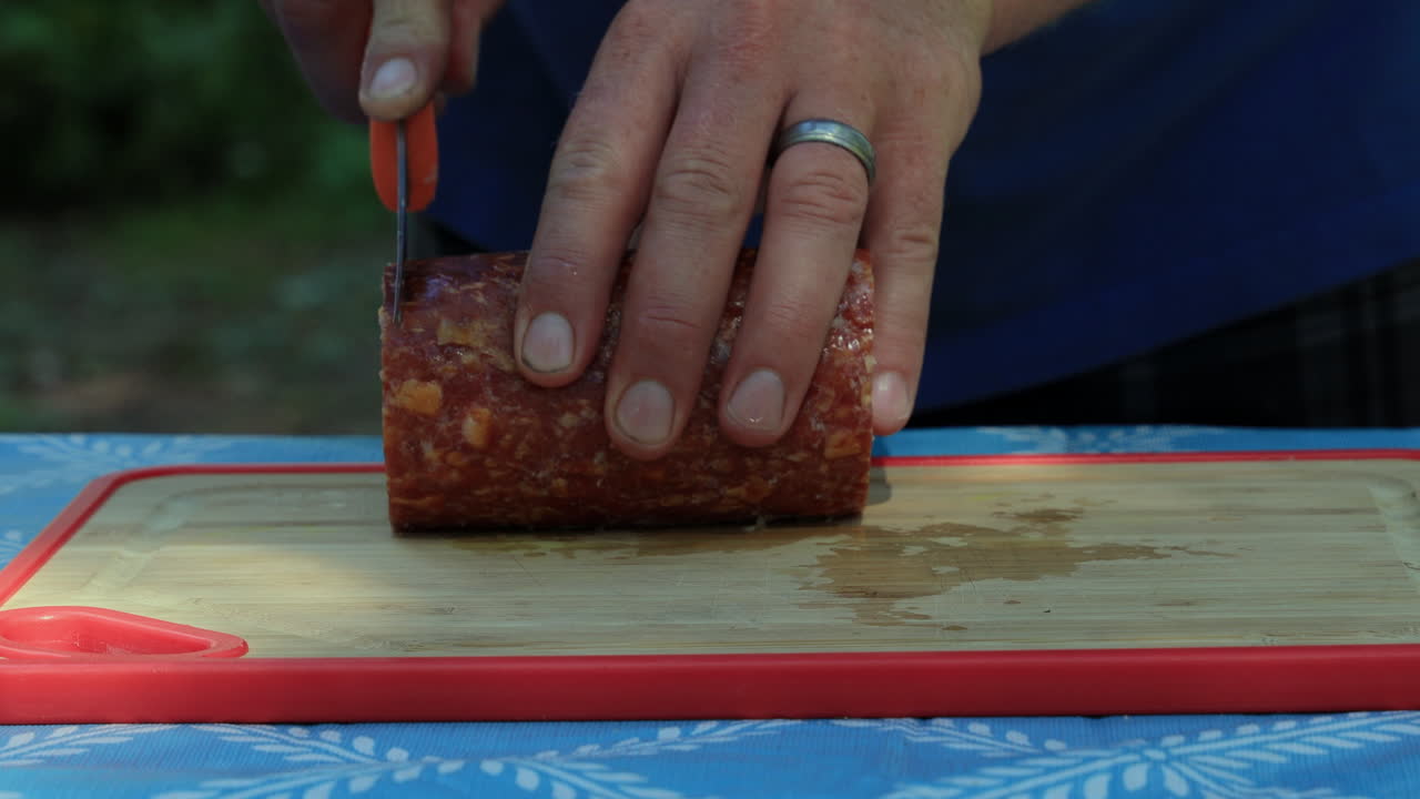 야외 요리를 위해 칼로 살라미 소시지를 자르는 캠퍼의 손