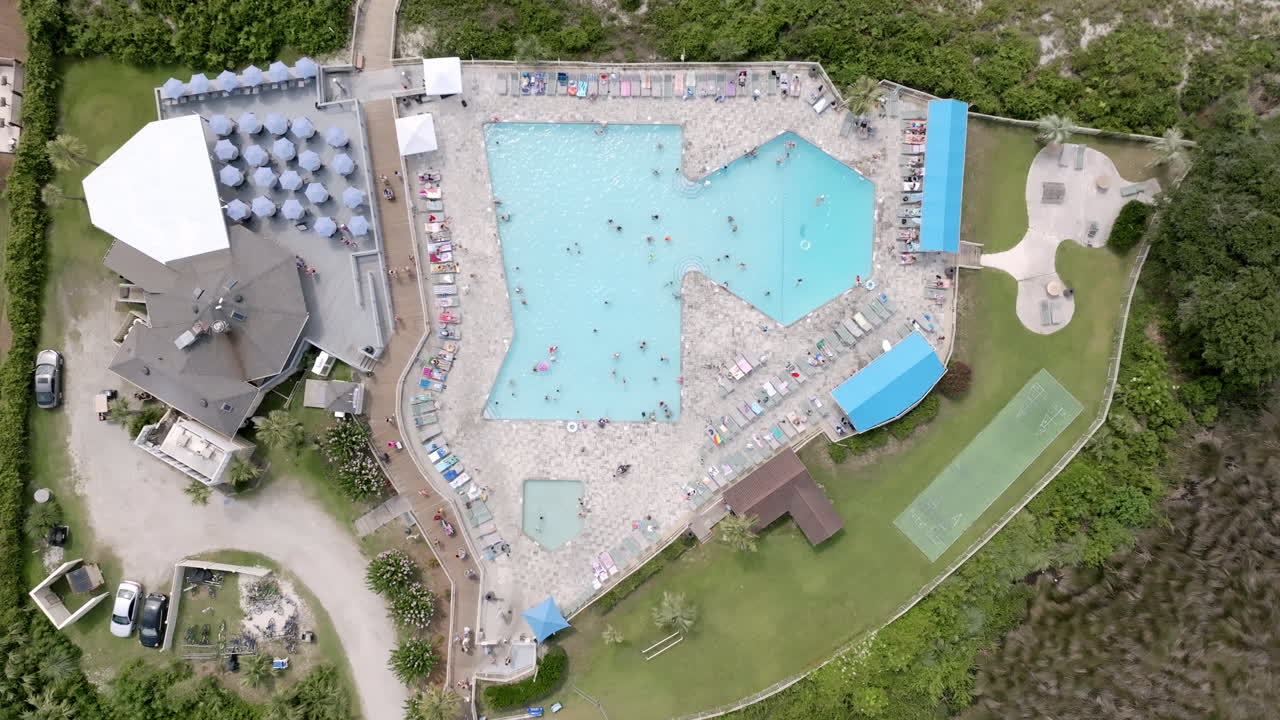 Bird’s-eye view of a large resort pool with umbrellas and lounge chairs, surrounded by walkways and lush greenery