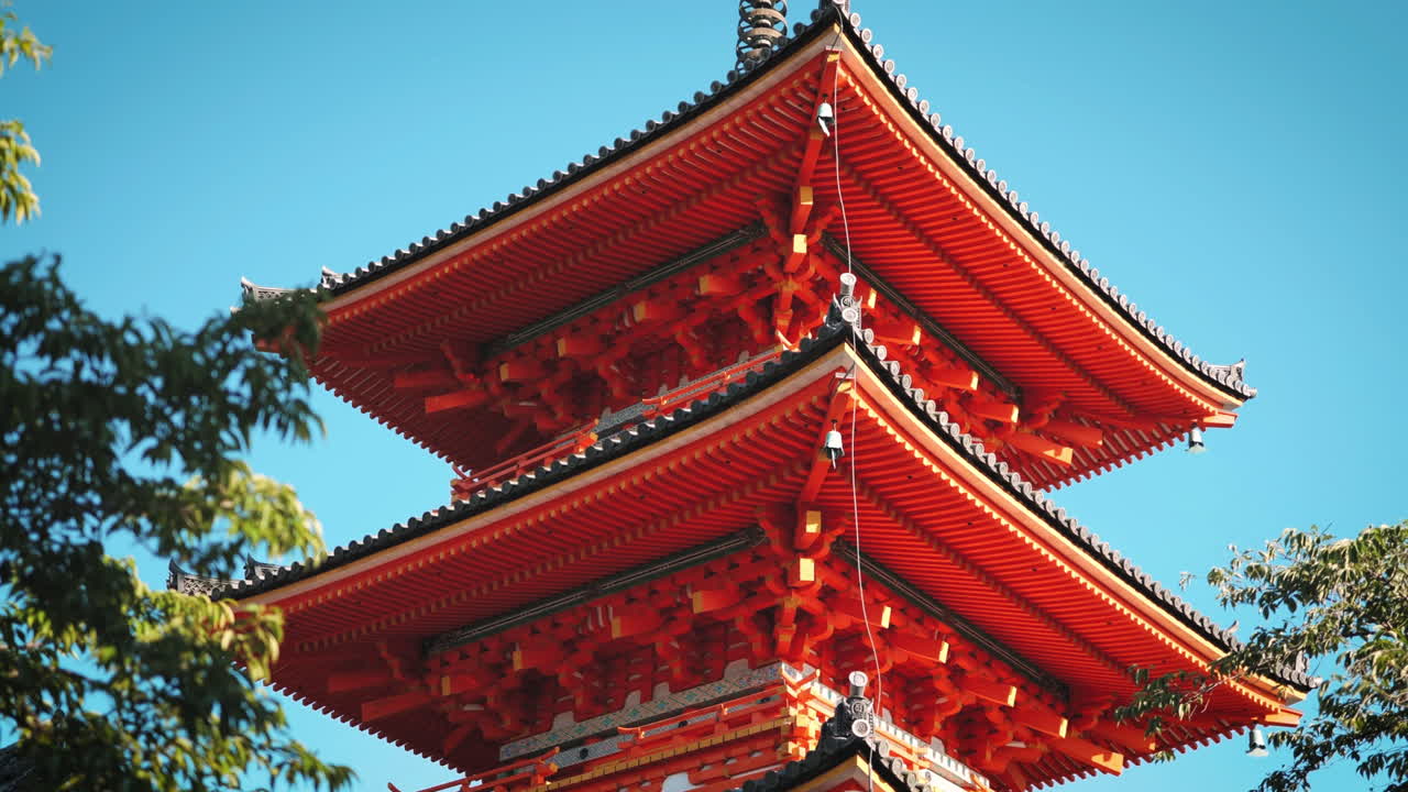 vista completa de la pagoda de tres niveles en el templo de kiyomizu-dera, kyoto, detalles rojos vibrantes contra el cielo azul claro, la arquitectura tradicional japonesa está rodeada de vegetación, significado cultural