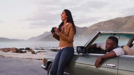 mujer afroamericana usando una cámara digital para tomar fotos mientras estaba de pie cerca del coche convertible