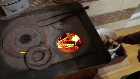 woman in the house putting pieces of wood into a wood stove through its round hole