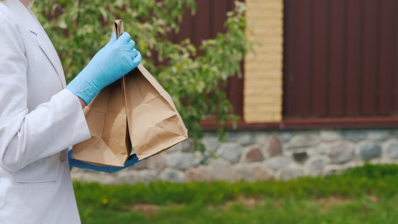 마스크와 장갑을 끼고 음식 가방을 집으로 운반하는 여성의 측면