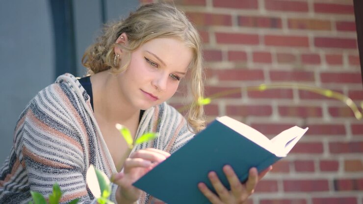 Close up of girl student reading a book outside of a school building
