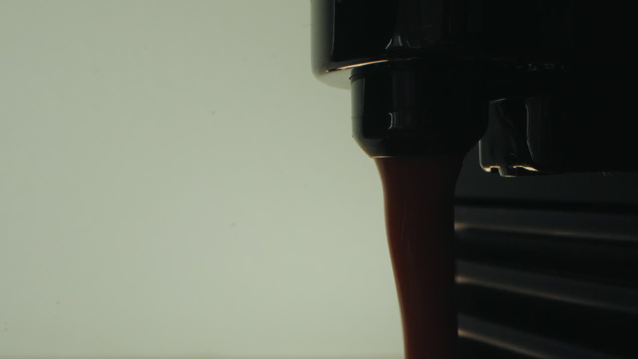 Dark coffee dripping from an espresso machine with a clean white background