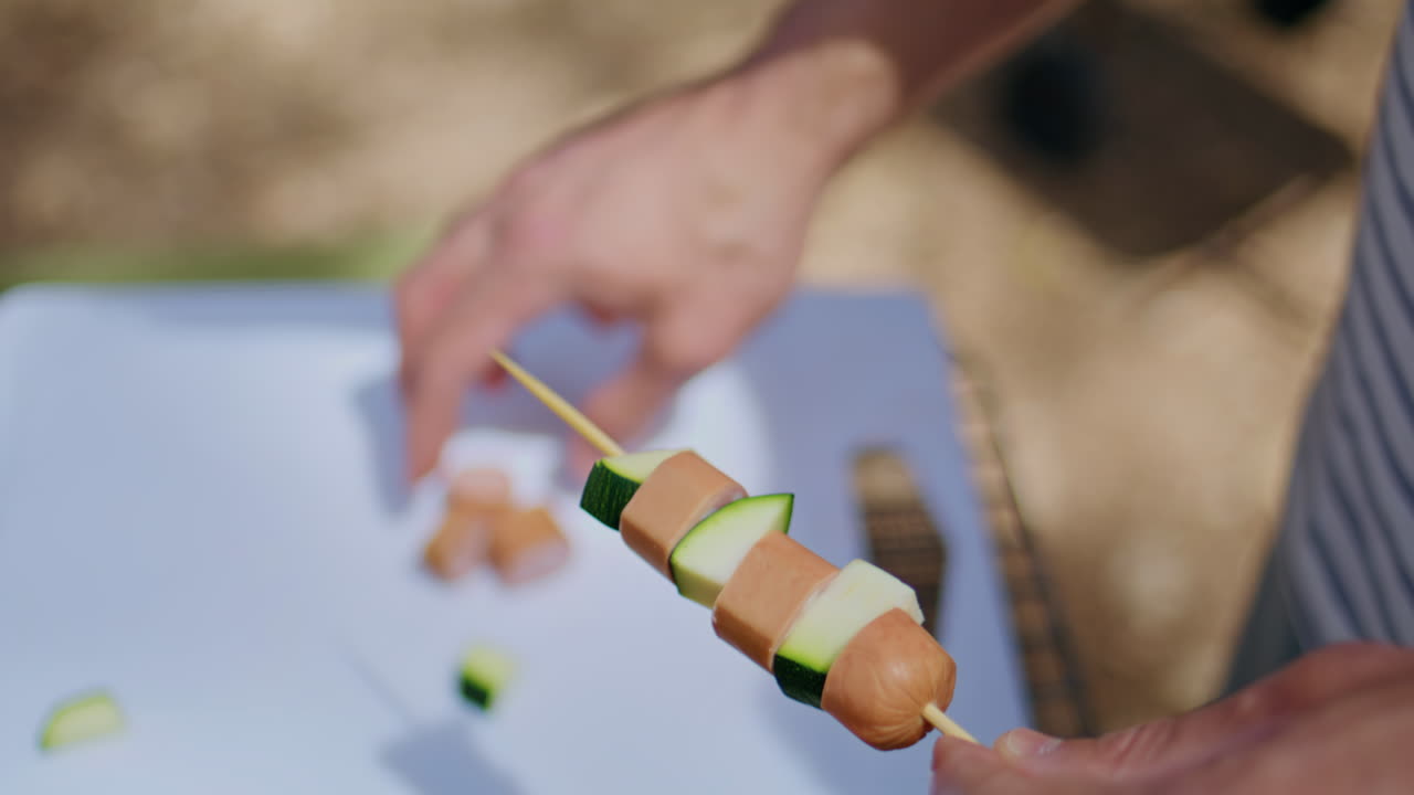 Man hands assembling food on skewer cooking outdoors closeup. Unknown young guy