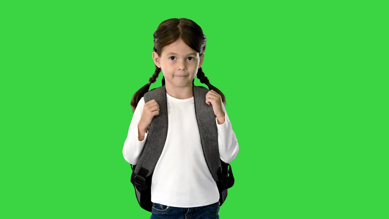 Smiling little girl walking to school holding her backpack and looking at camera on a Green Screen, Chroma Key
