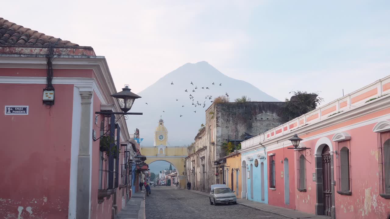 En fugleflok flyver glædeligt rundt på himlen omkring Santa Catalinas gule klokketårnsbue i Antigua, Guatemala.