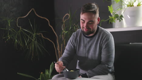 hungry man sitting on sofa and eating delicious noodles