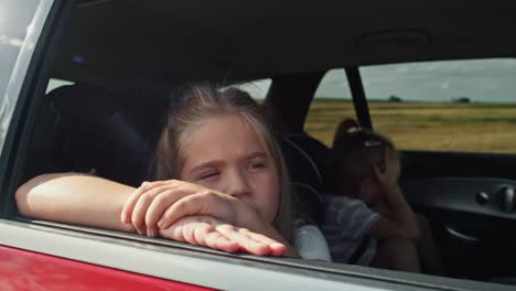 caucasian girl of 8 years looking out of the car window while car trip and her sister in the background.