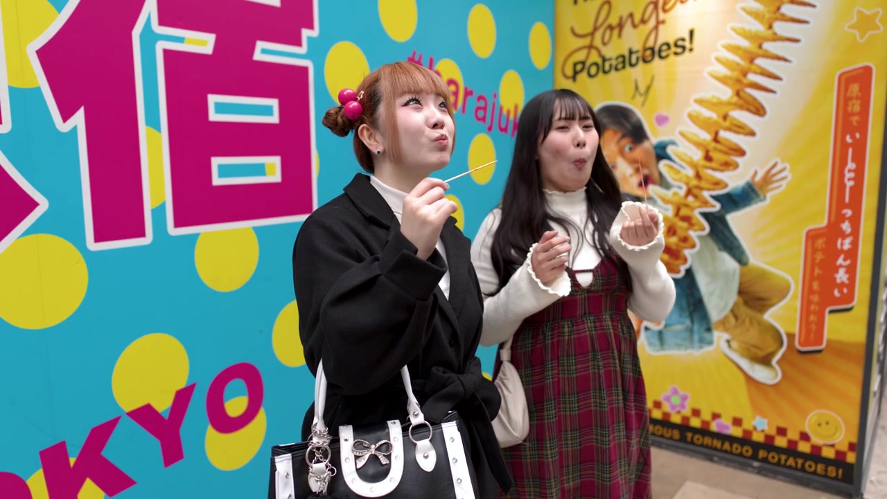 鮮やかでカラフルな都会の背景を背に、砂糖漬けのフルーツ串を食べるおしゃれな若い女性二人。