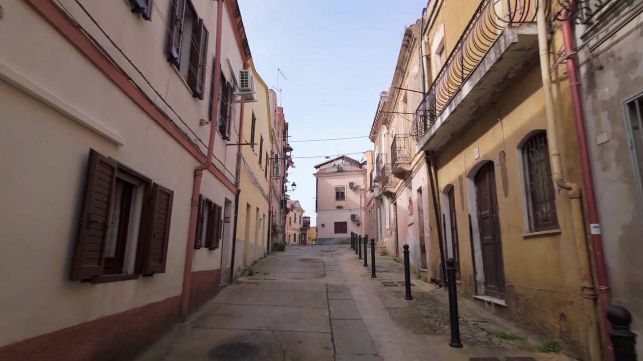 Una calle estrecha en Iglesias, Cerdeña, Italia, mostrando fachadas de piedra, casas y el paisaje urbano tradicional del pueblo.