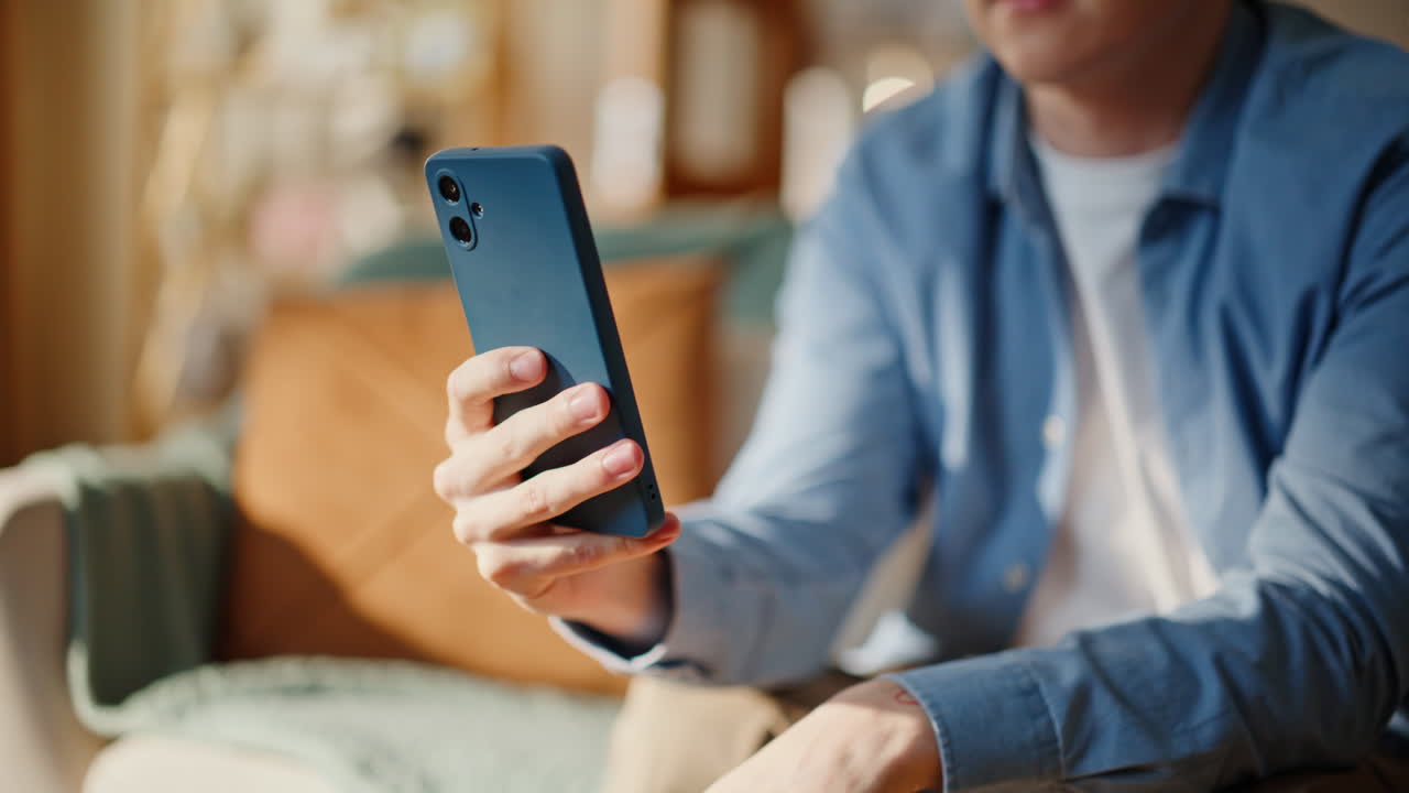 Primo piano di un uomo che tiene in mano uno smartphone e saluta durante una riunione online con un amico in un ambiente interno