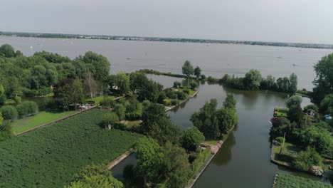 aerial slomo shot of green dutch countryside with small boats, streams and lake, during sunny weather and small town in background