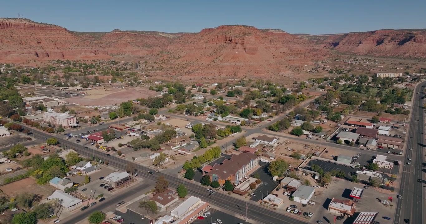Strade residenziali ed edifici di Kanab, Utah, con scogliere di arenaria rossa sullo sfondo, ripresa aerea con inclinazione verso l'alto.