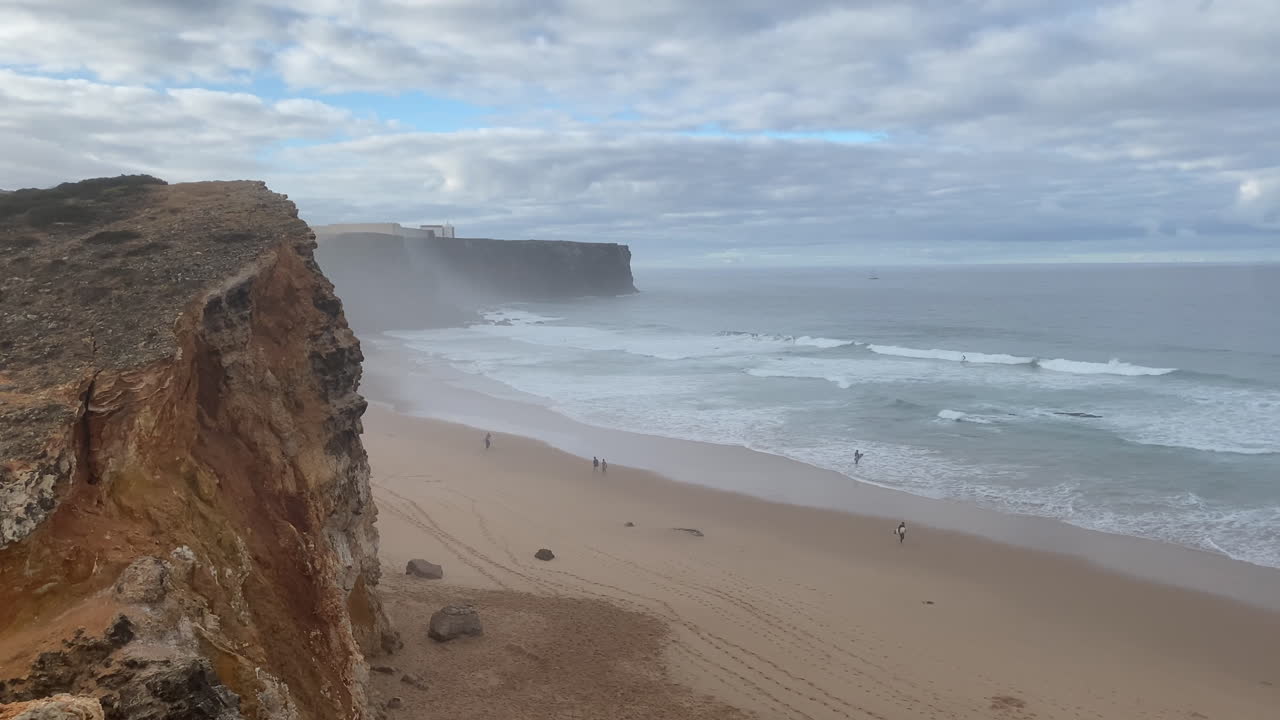 The Sagres lighthouse stands far beyond the cliffs, guiding sailors through the calm Atlantic waters