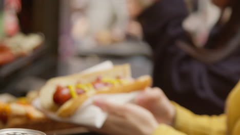 close up of two women buying hot dogs from street food market stall