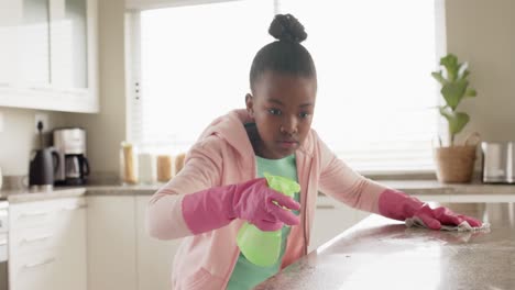 Happy-african-american-girl-cleaning-countertop-in-kitchen,-in-slow-motion