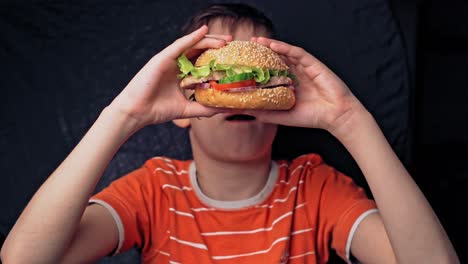 Young happy teenager eating tasty hamburger. Delicious grilled burger