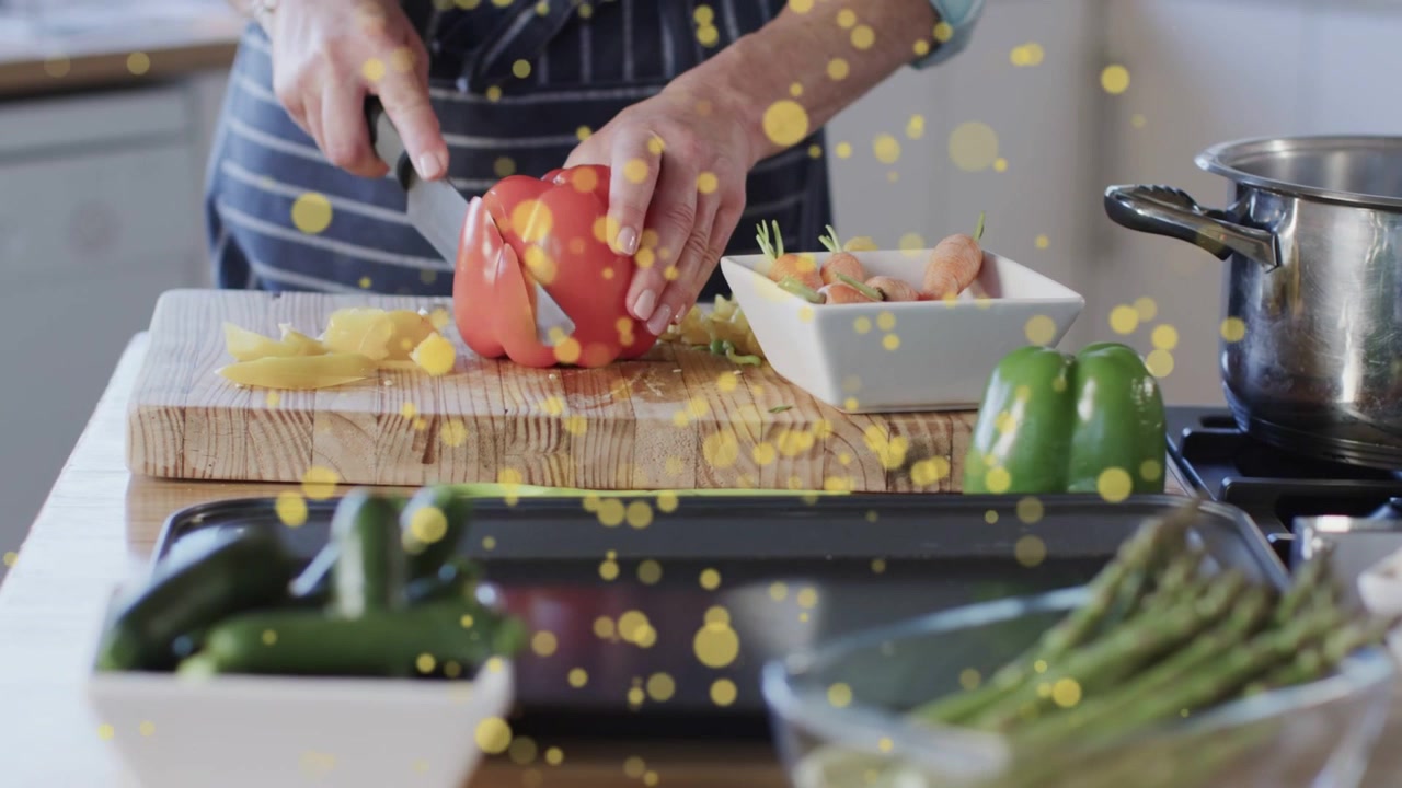 Cuoco che posiziona un peperone rosso sul tagliere, tagliandolo a cubetti, preparando il pasto mentre un bokeh giallo oscura le mani.