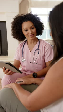 vertical video: nurse in pink scrubs using tablet, discussing health information with patient