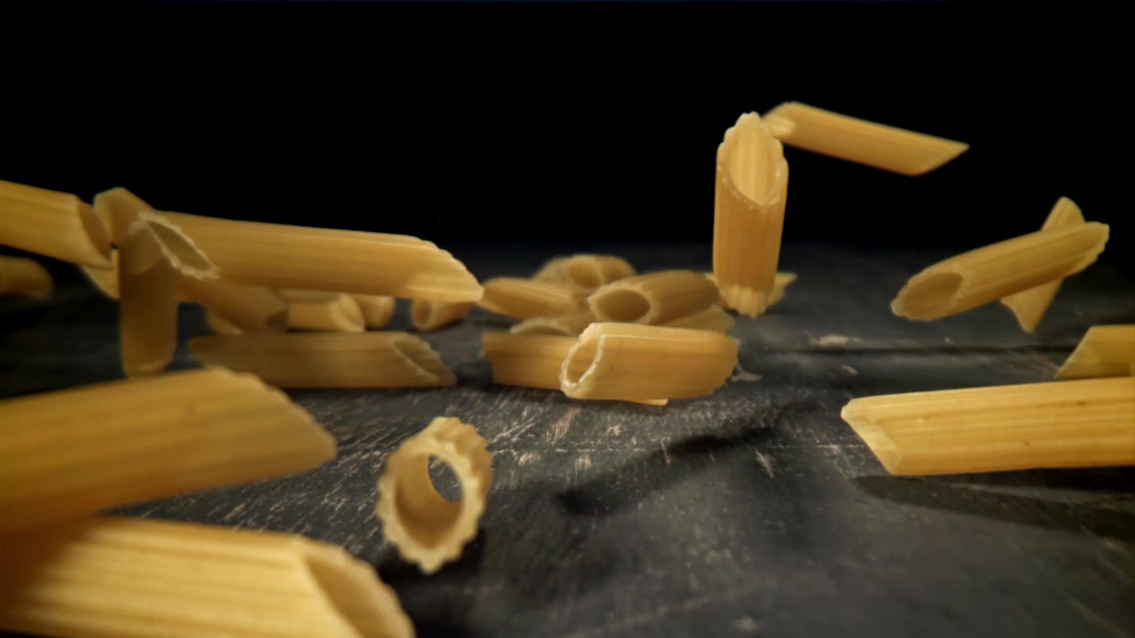 Penne che cadono al rallentatore su una superficie scura