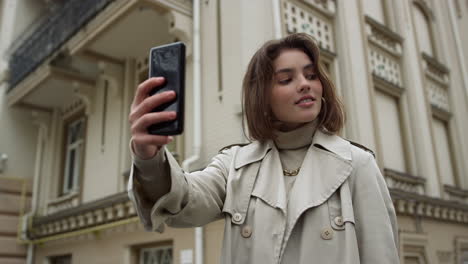 una mujer sonriente tomando una selfie en una calle urbana. una chica con los labios fruncidos para la cámara del teléfono.