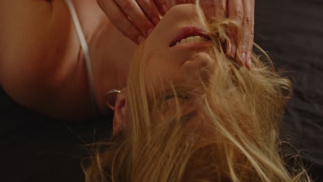 Beautiful-close-up-of-an-attractive-woman-lying-in-bed-throwing-her-long-blond-hair-in-front-of-her-face-in-slow-motion-and-caressing-her-face